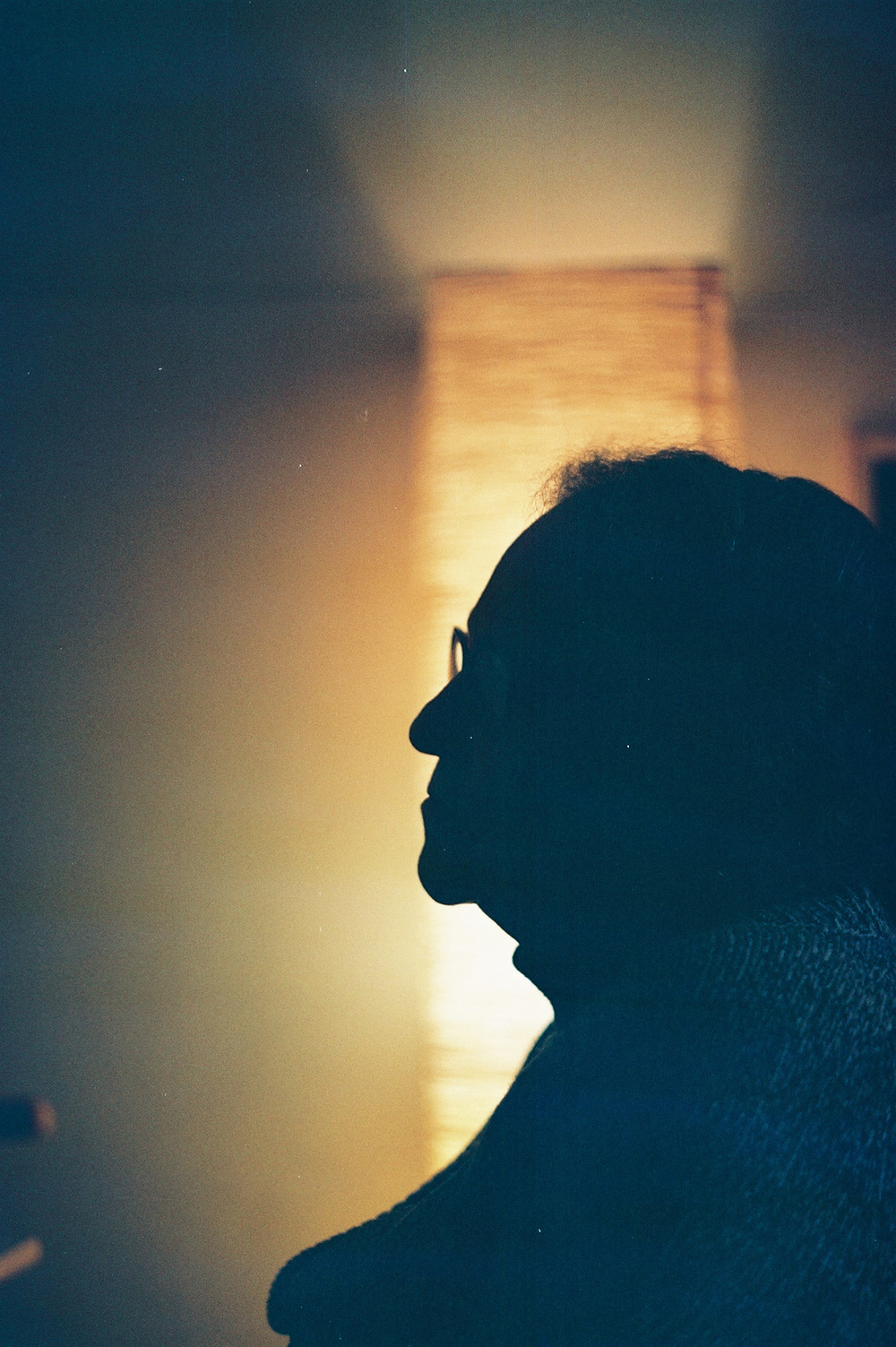 Analog photo of a woman's profile silhouetted against a lamp behind her.