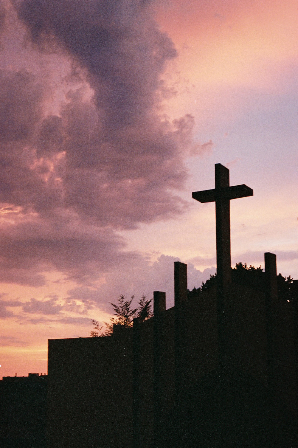 Analog photo of a church's cross silhouetted against a pink sky.