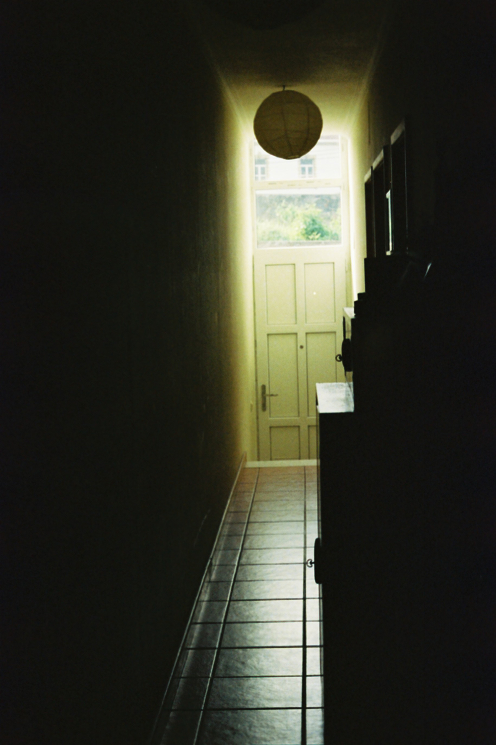 Analog photo of a long, dark and narrow hallway, with light coming from a small window at the end.