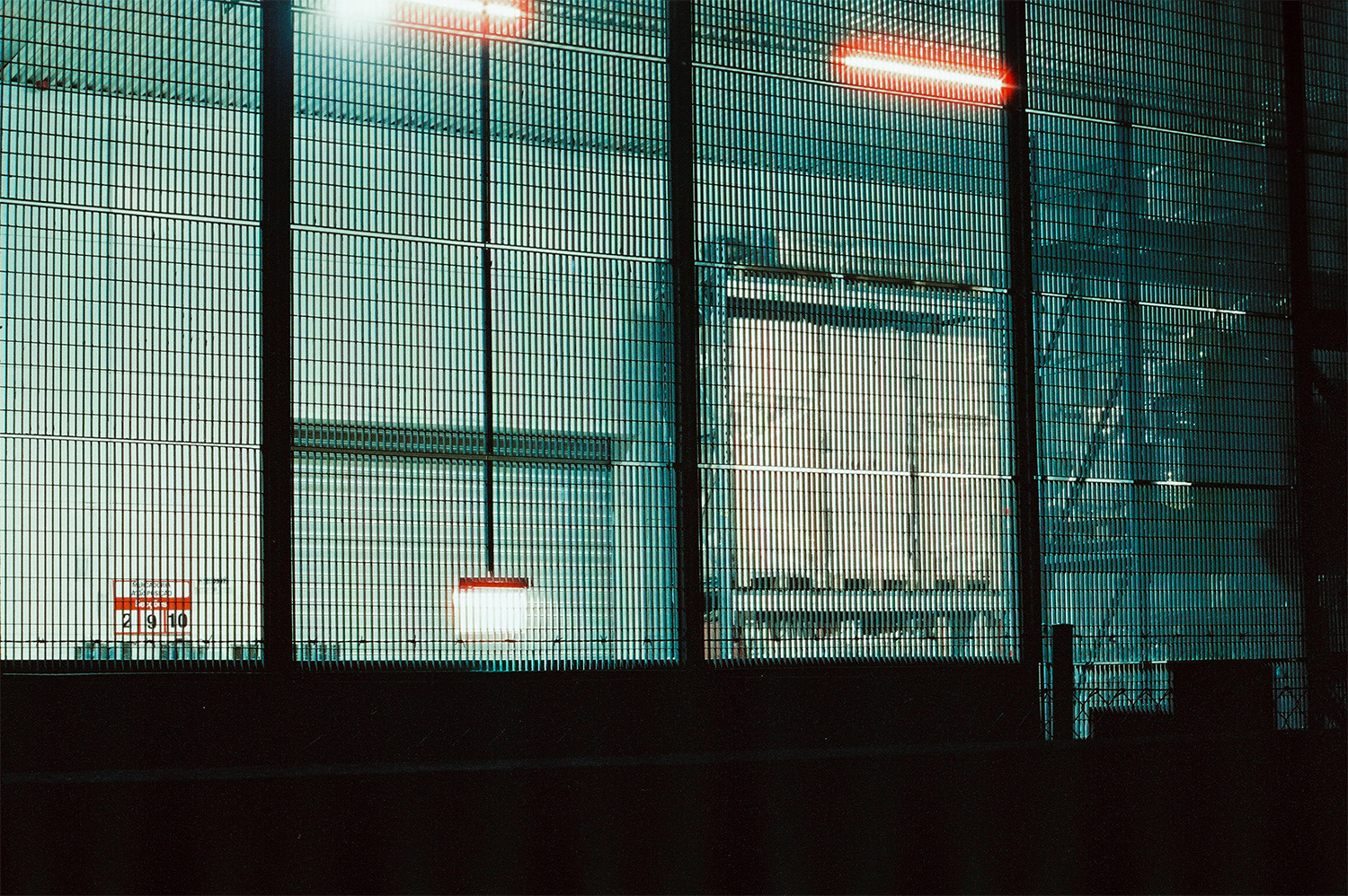 Analog photo of the inside of warehouse through a fence at night.